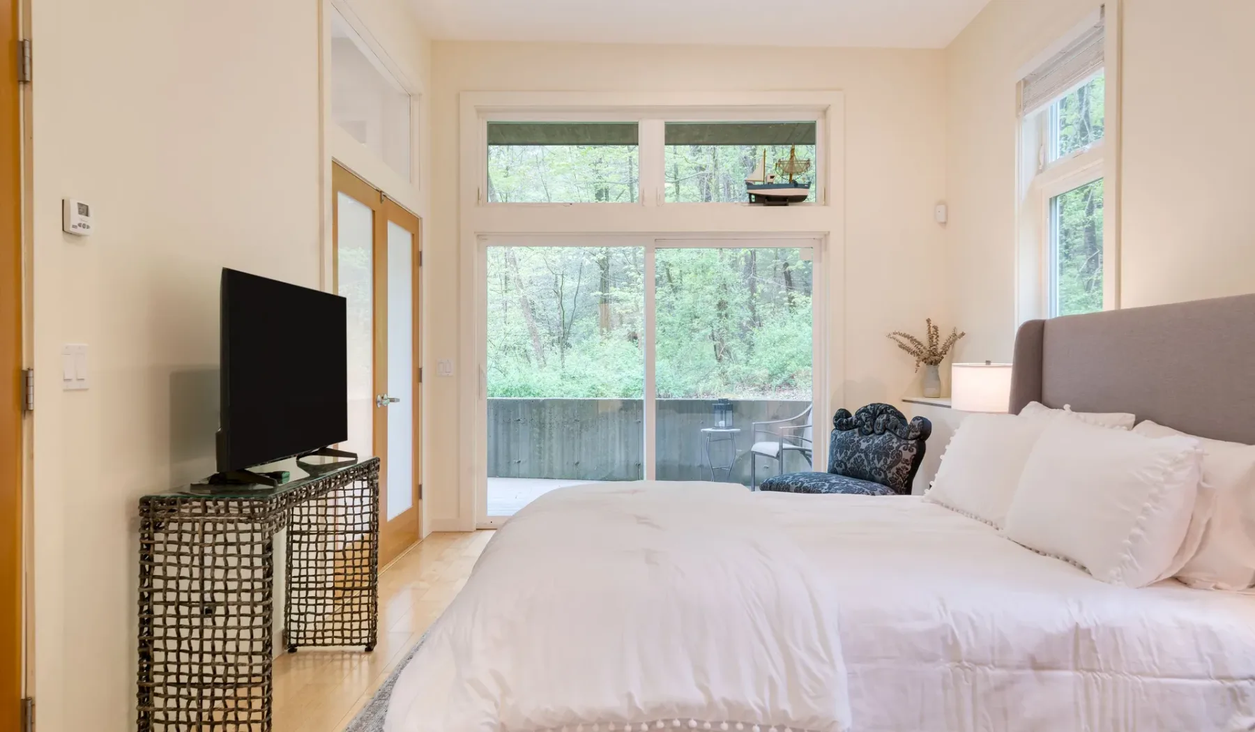 A bright bedroom with a large bed and windows overlooking trees.
