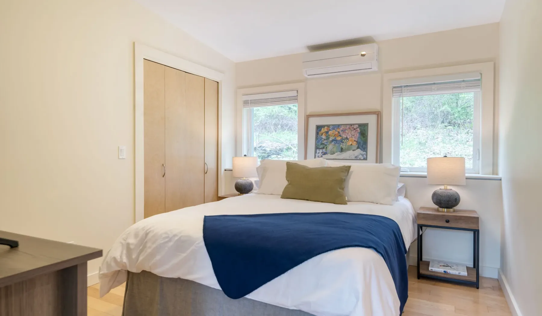 A bright bedroom with a neatly made bed between two windows.