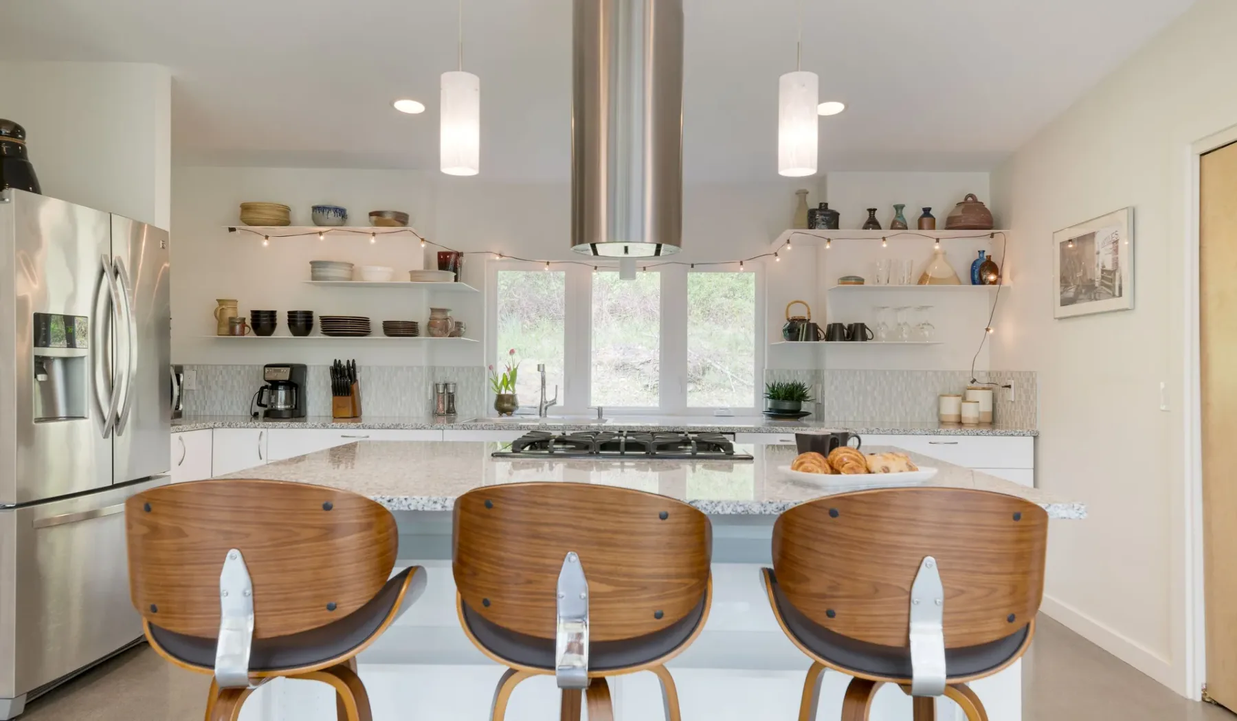 A bright kitchen with a central island and three wooden stools.
