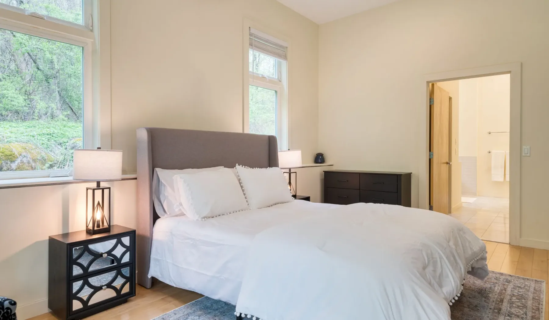 A bedroom with a bed beside tall windows and a doorway to a bathroom.