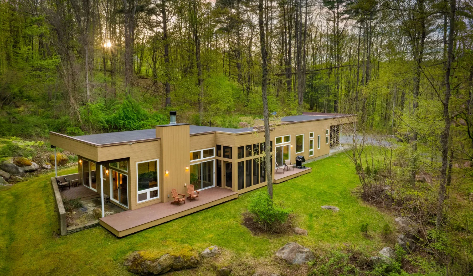 A modern house sits in a forest clearing beside a grassy lawn.
