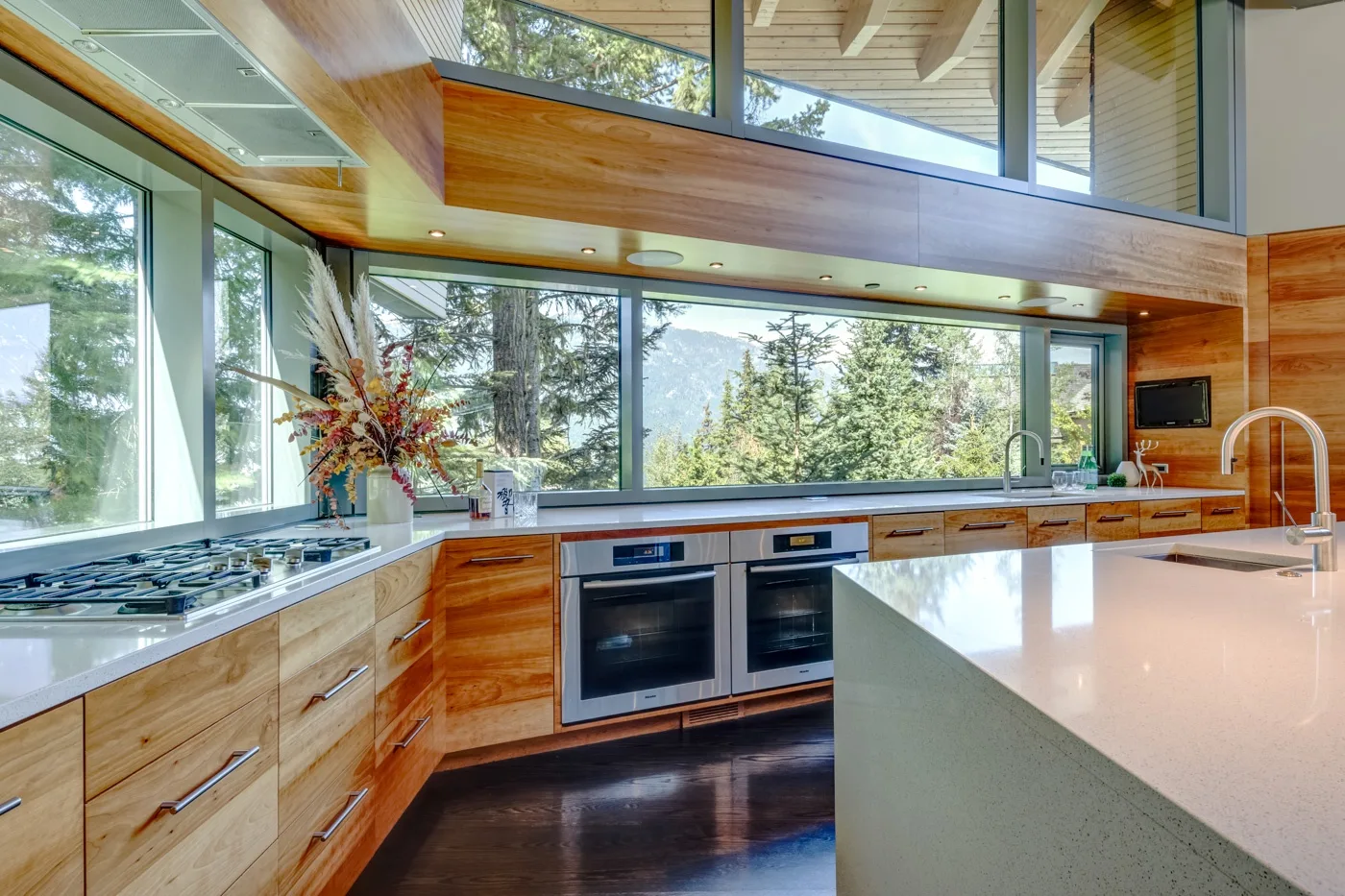 Una cocina moderna con gabinetes de madera, grandes ventanas y una isla luminosa.