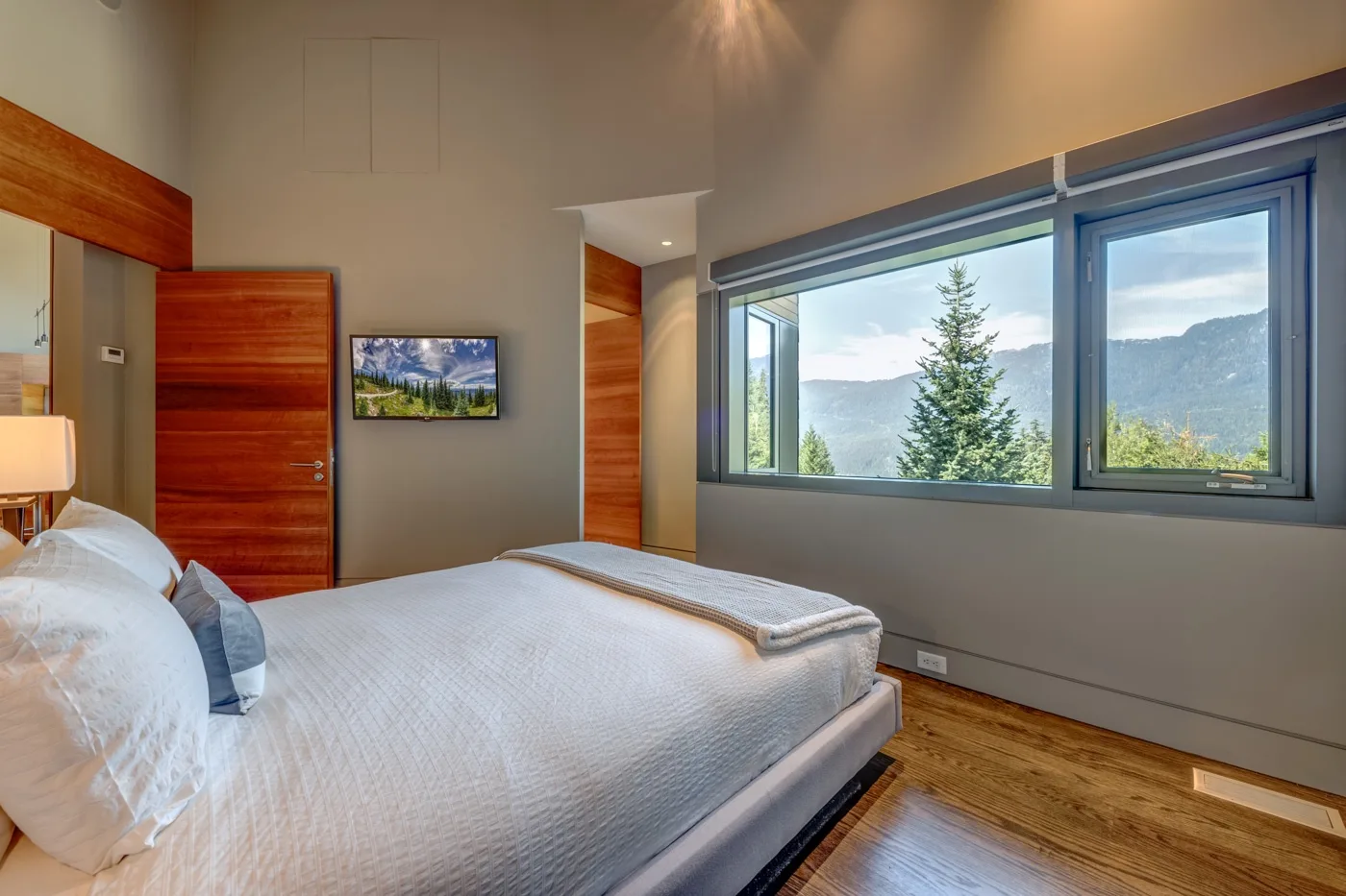 Un dormitorio con una cama junto a una ventana amplia con vistas a árboles y montañas.