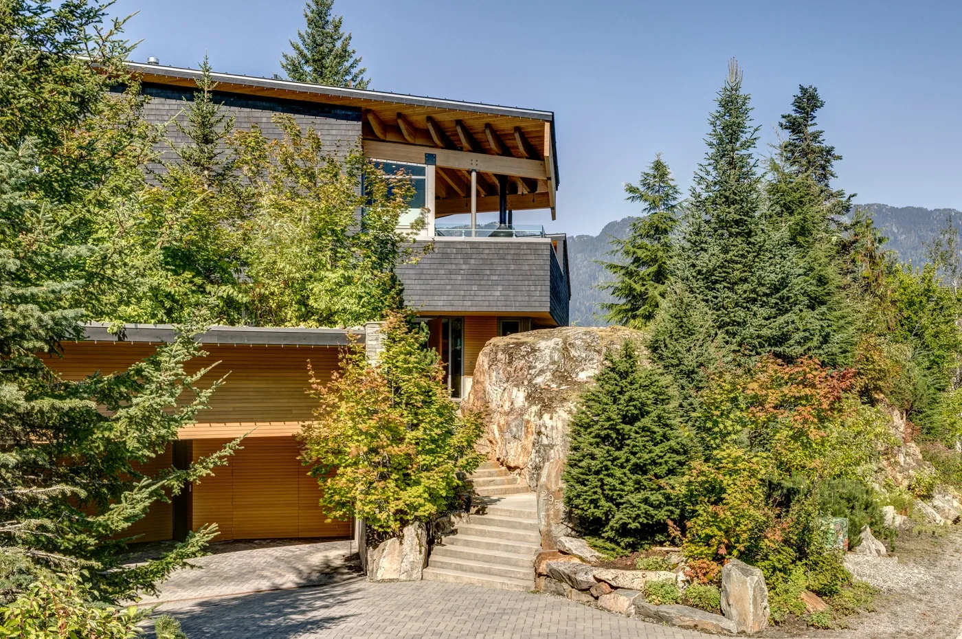Una casa moderna entre árboles de hoja perenne, con escalones de piedra hacia la entrada.