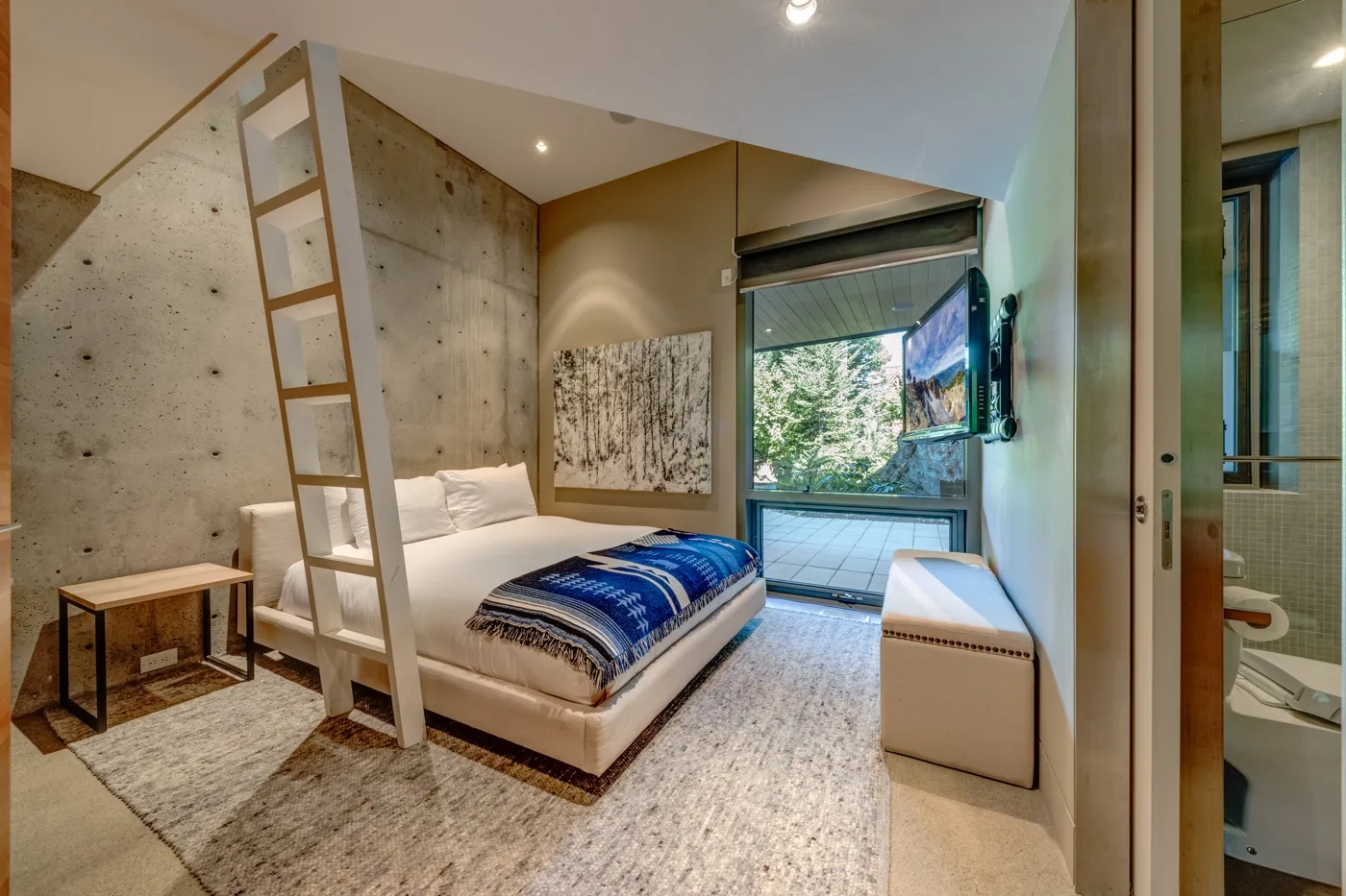 Un dormitorio con una cama, una escalera y una ventana grande con vista a la vegetación.