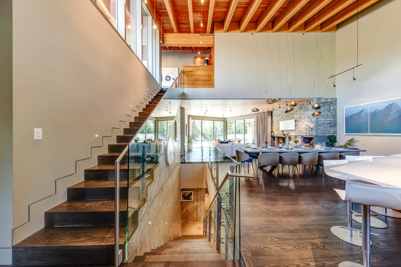 Comedor moderno de planta abierta junto a una escalera, con una mesa larga y lámparas colgantes.