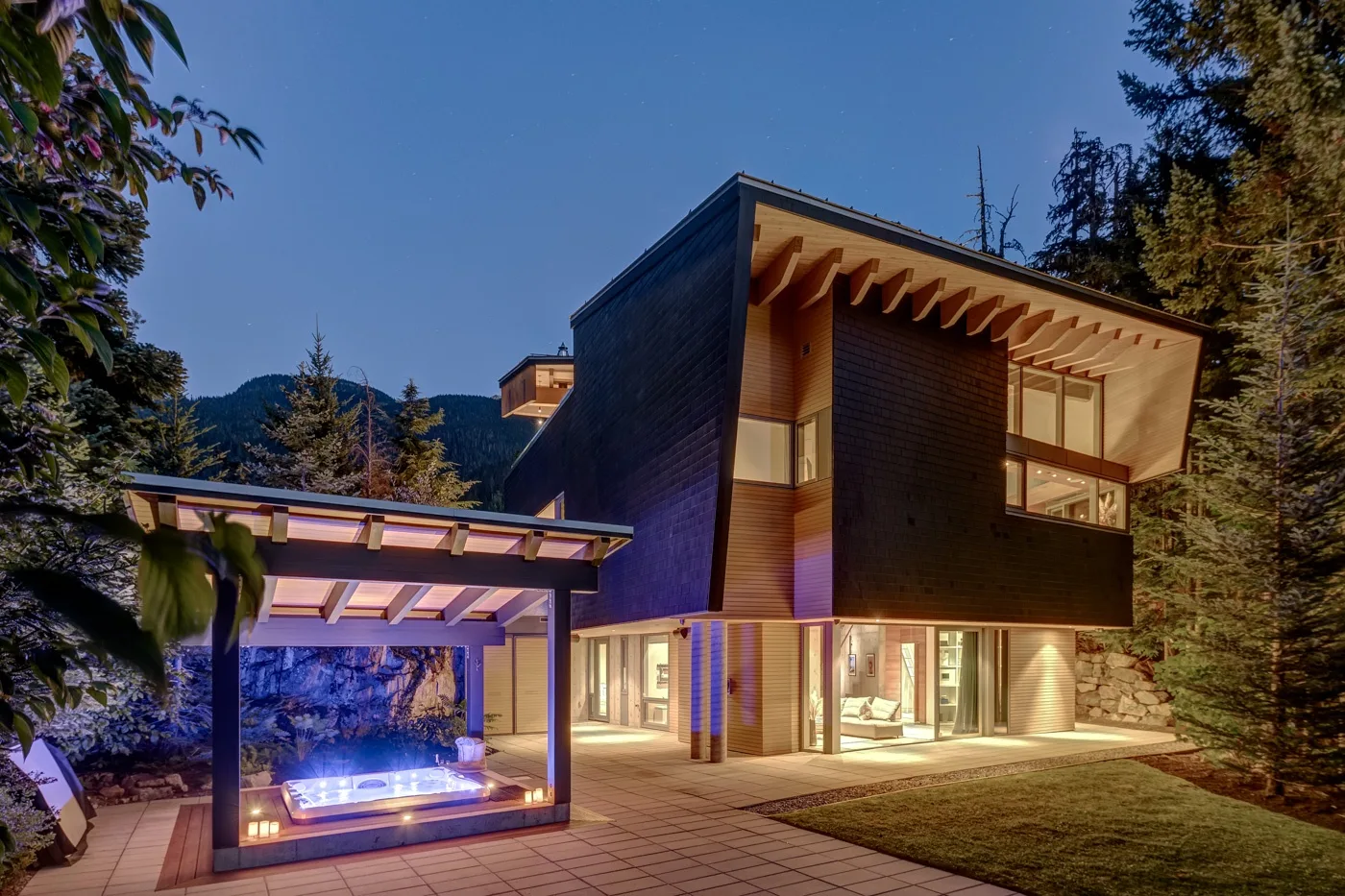 Una casa moderna al anochecer, con grandes ventanales y una zona exterior para sentarse.
