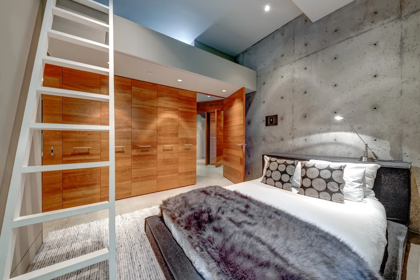 Dormitorio moderno con cama blanca, armarios de madera y una pared de concreto.
