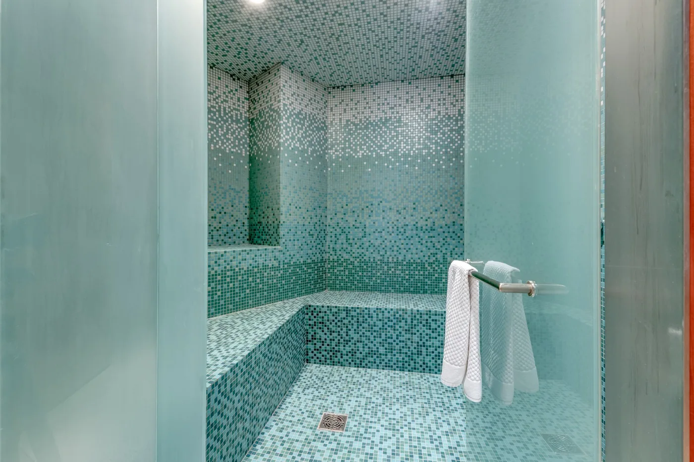 Una ducha con azulejos, un borde integrado y toallas colgadas cerca.
