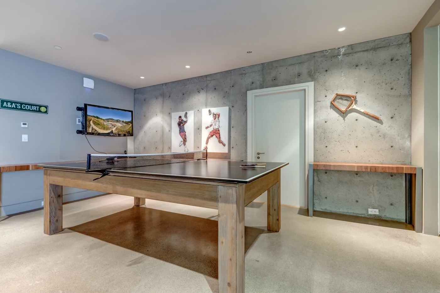 Una sala de recreación con una mesa de ping-pong, un televisor en la pared y paredes de concreto.