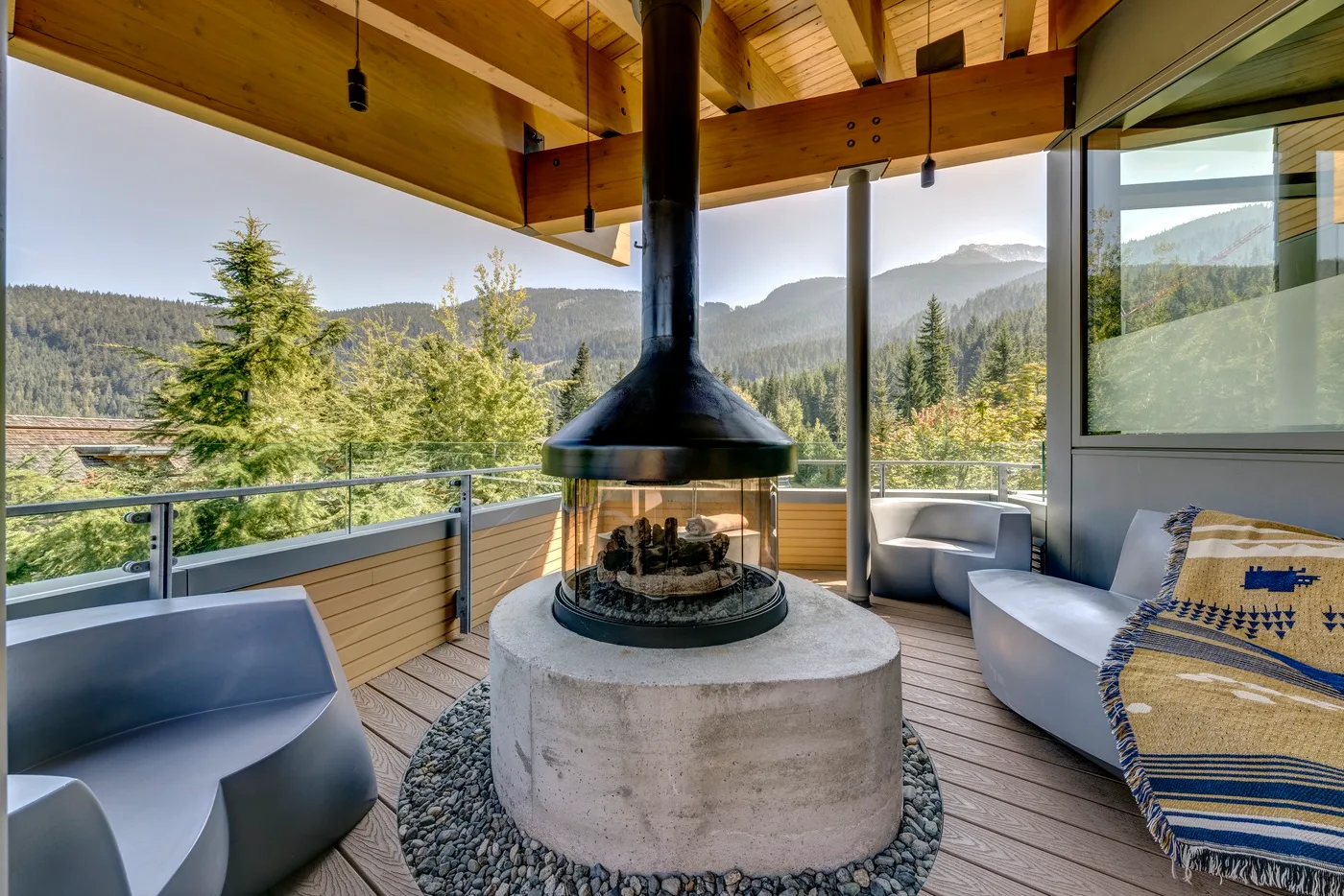 Una sala acristalada con asientos alrededor de una chimenea central, con vistas a colinas boscosas.