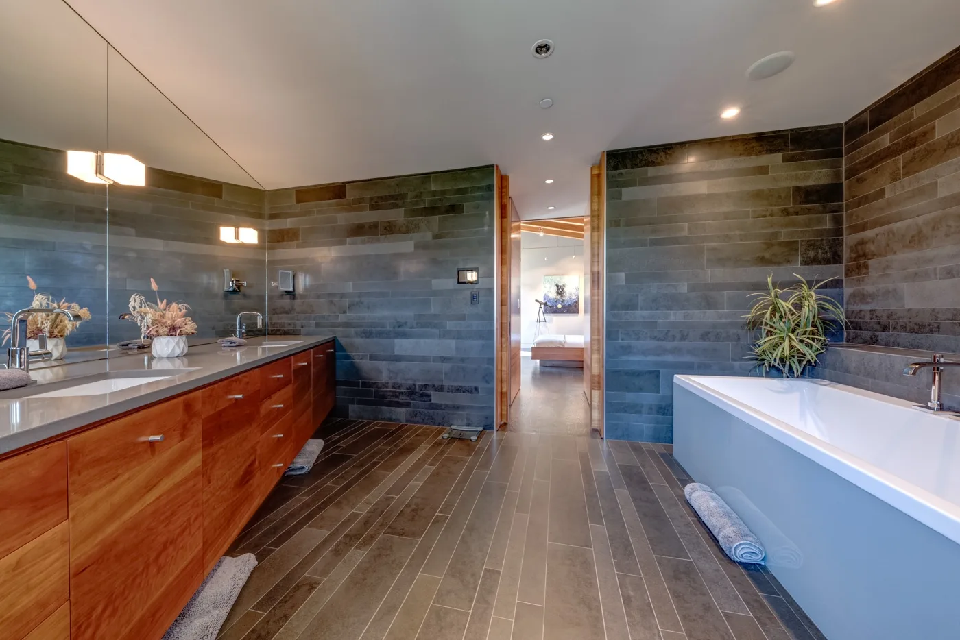 Un baño amplio con un tocador largo, una bañera y paredes de azulejos oscuros.