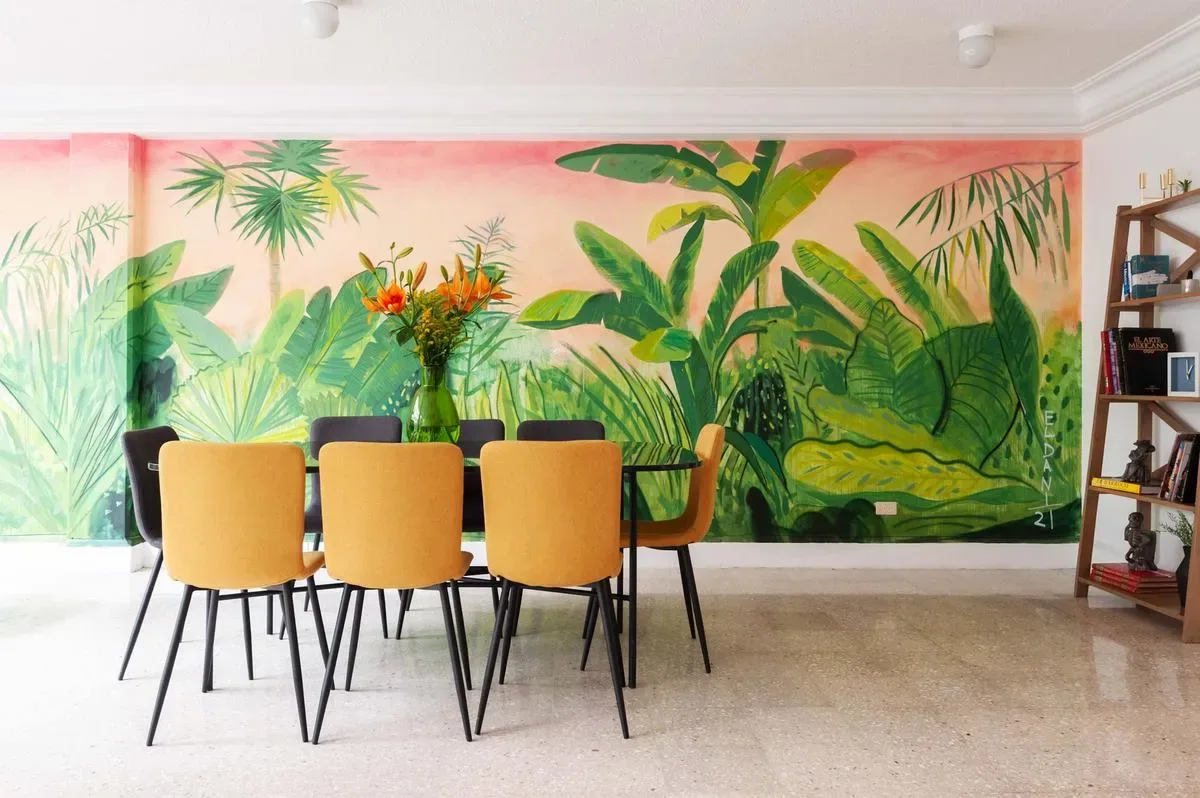 Dining area with a black table, mustard chairs, and a colorful tropical mural across the wall.