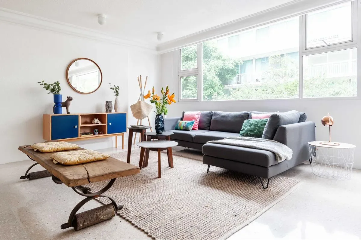 A bright living room features a gray sectional sofa, a rustic wooden coffee table, and large windows.
