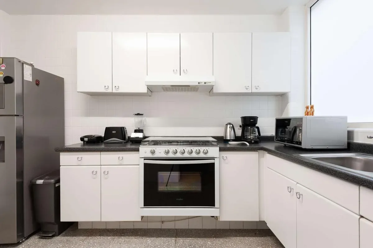 A bright white kitchen with overhead cabinets, a stove and oven, countertop appliances, and a tall refrigerator.