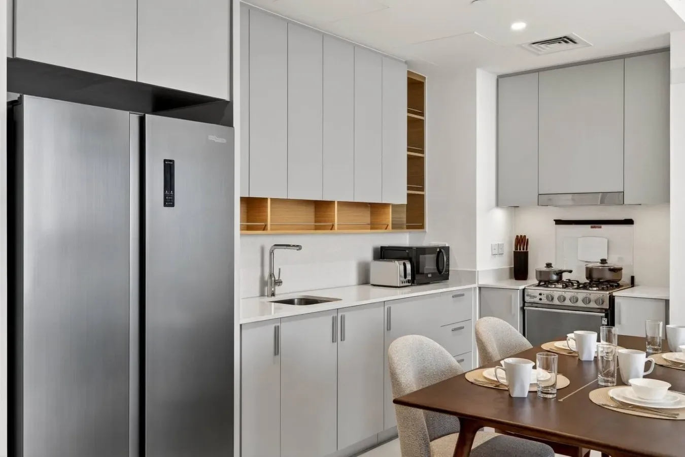 Una cocina moderna con gabinetes claros, un refrigerador grande y una mesa de comedor.