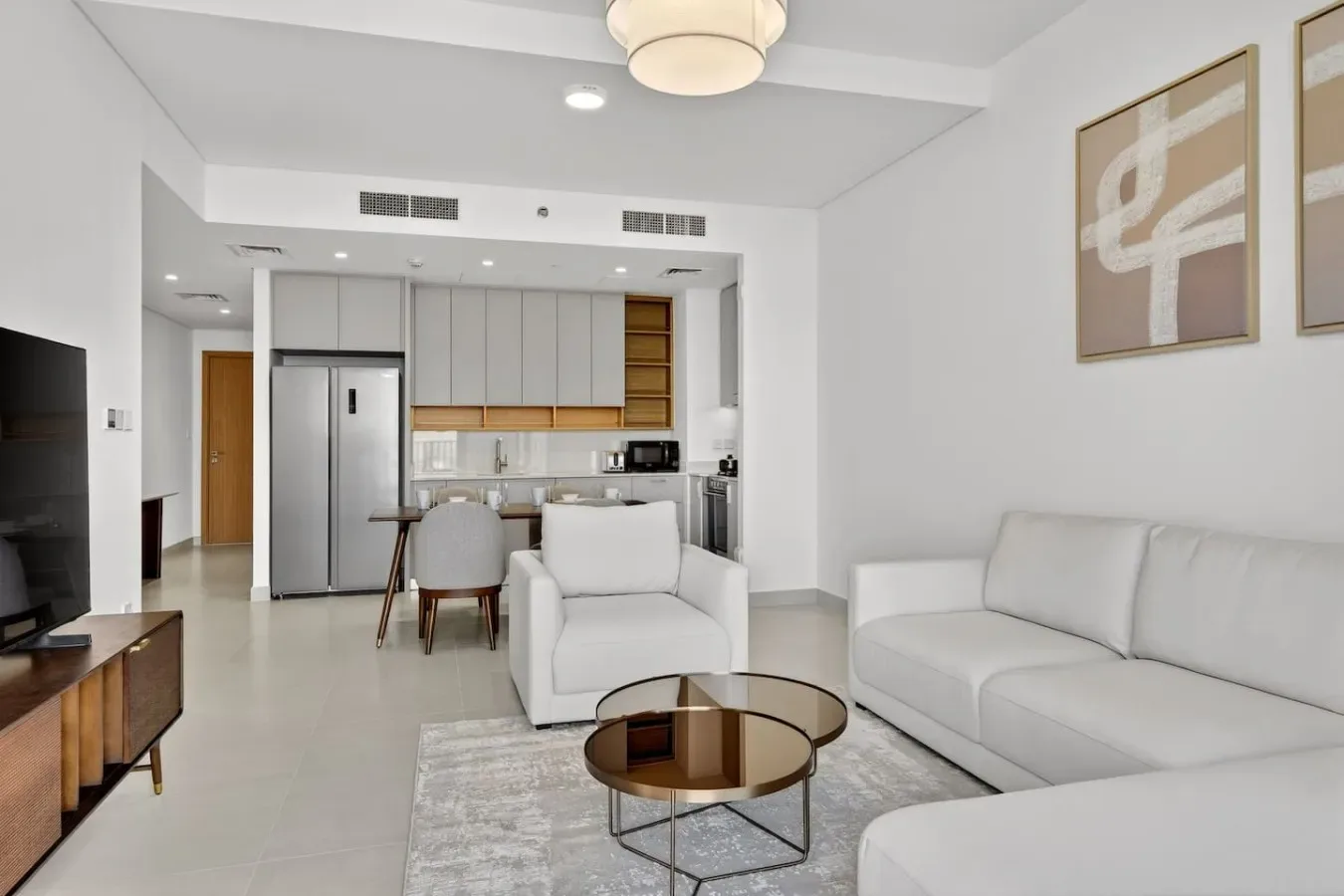 Una sala luminosa se abre a una cocina, con asientos claros y un comedor.