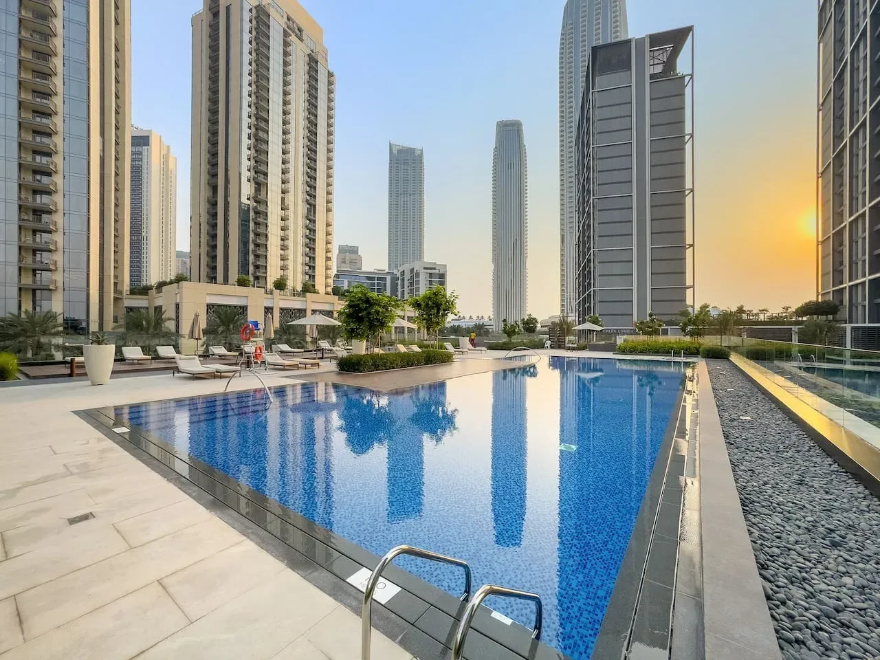 Una piscina al aire libre está rodeada de edificios altos bajo la luz cálida del atardecer.