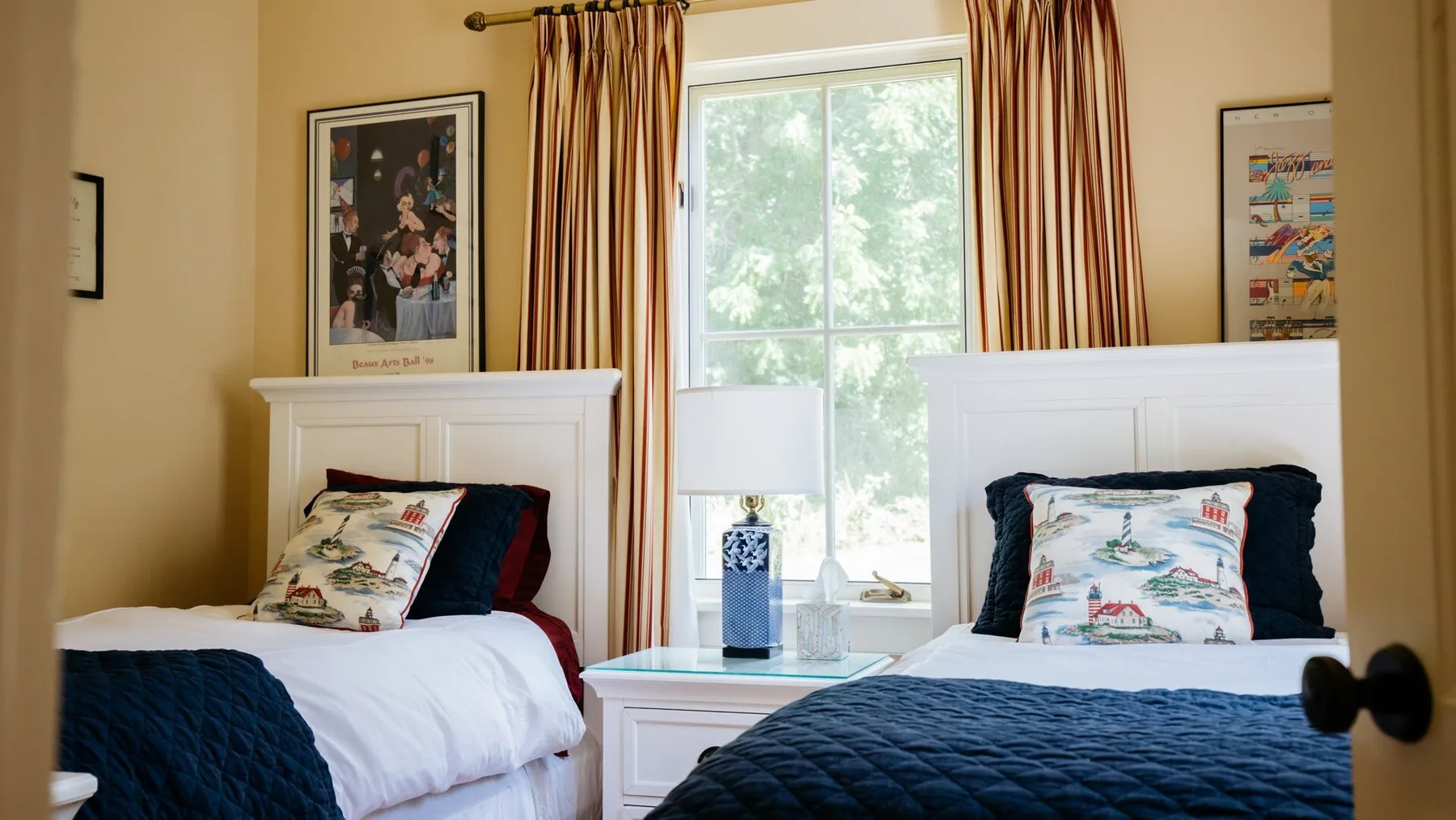 A bedroom with two beds, patterned pillows, and a window framed by striped curtains.