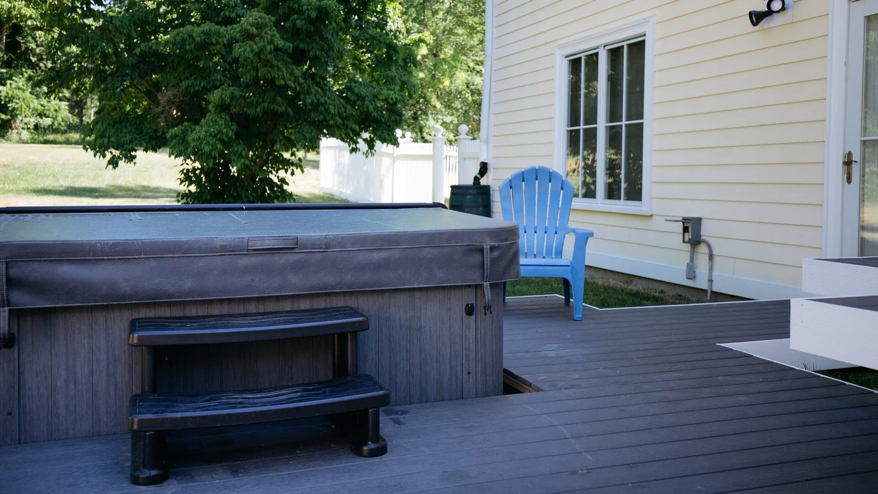 An outdoor hot tub sits beside a house on a wooden deck.