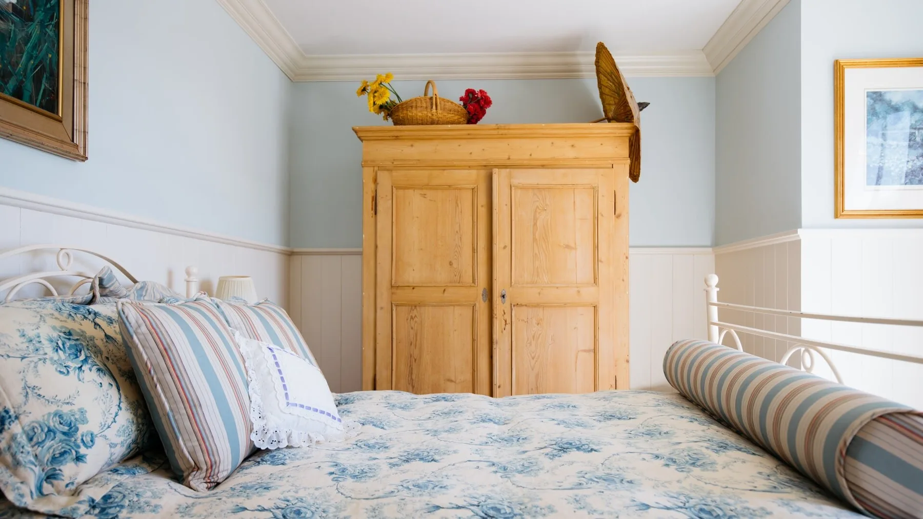 A bedroom with a floral bedspread and a wooden wardrobe.