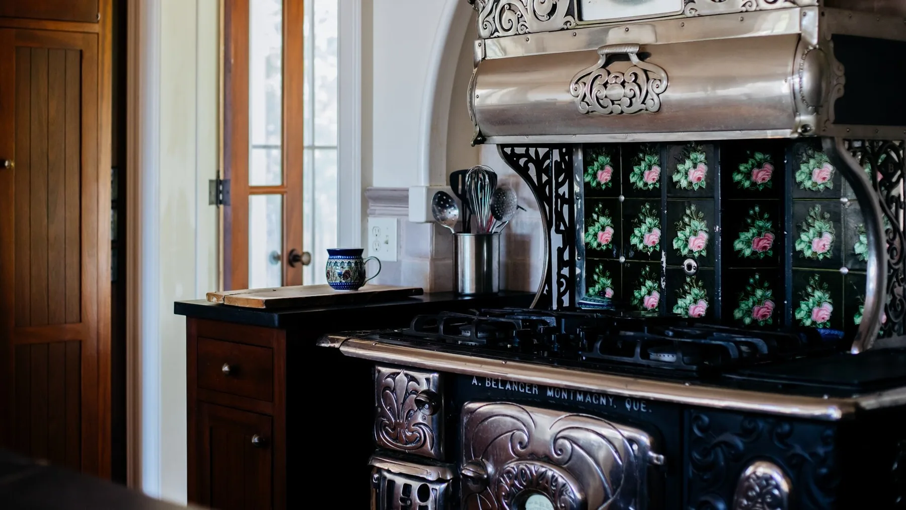A traditional kitchen with an ornate dark stove beneath a decorative metal hood.