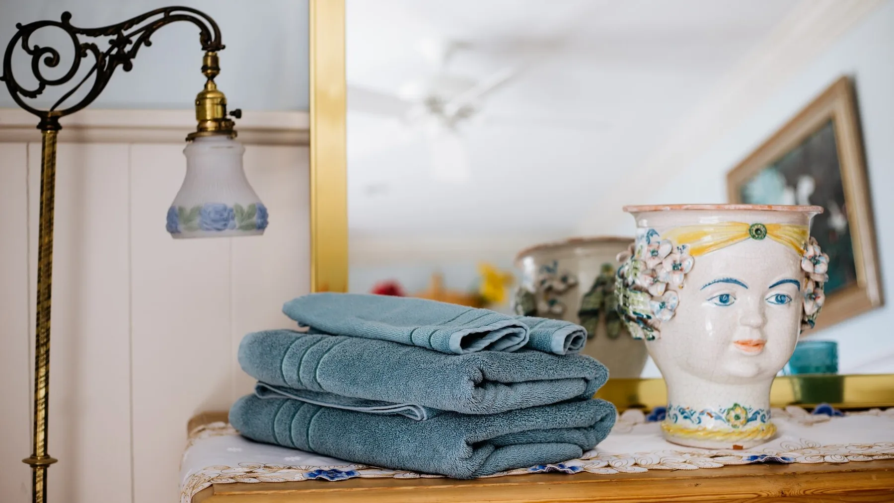 A room interior with folded towels beside a decorative ceramic vessel and standing lamp.