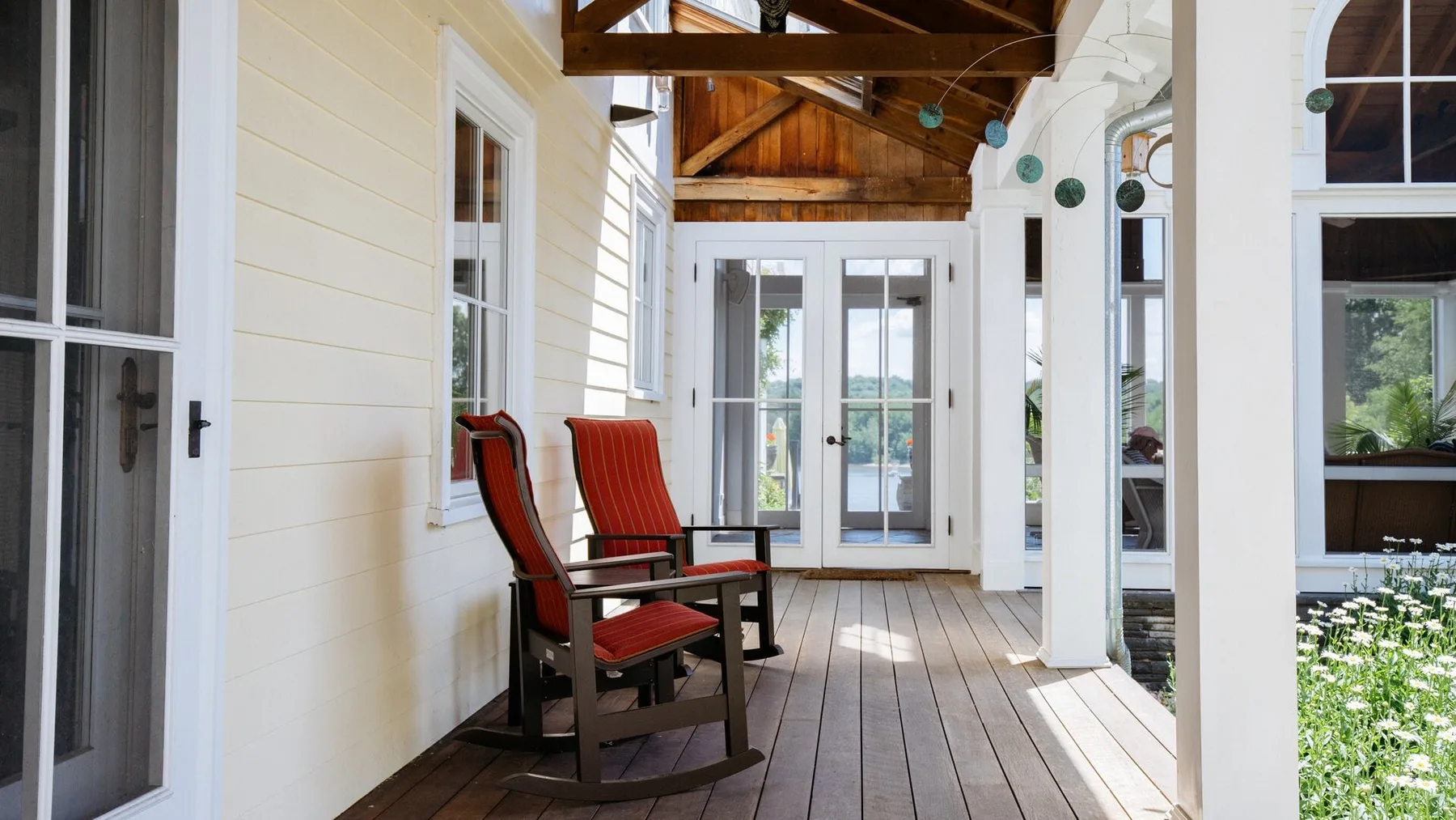 A covered porch with red rocking chairs and glass doors.