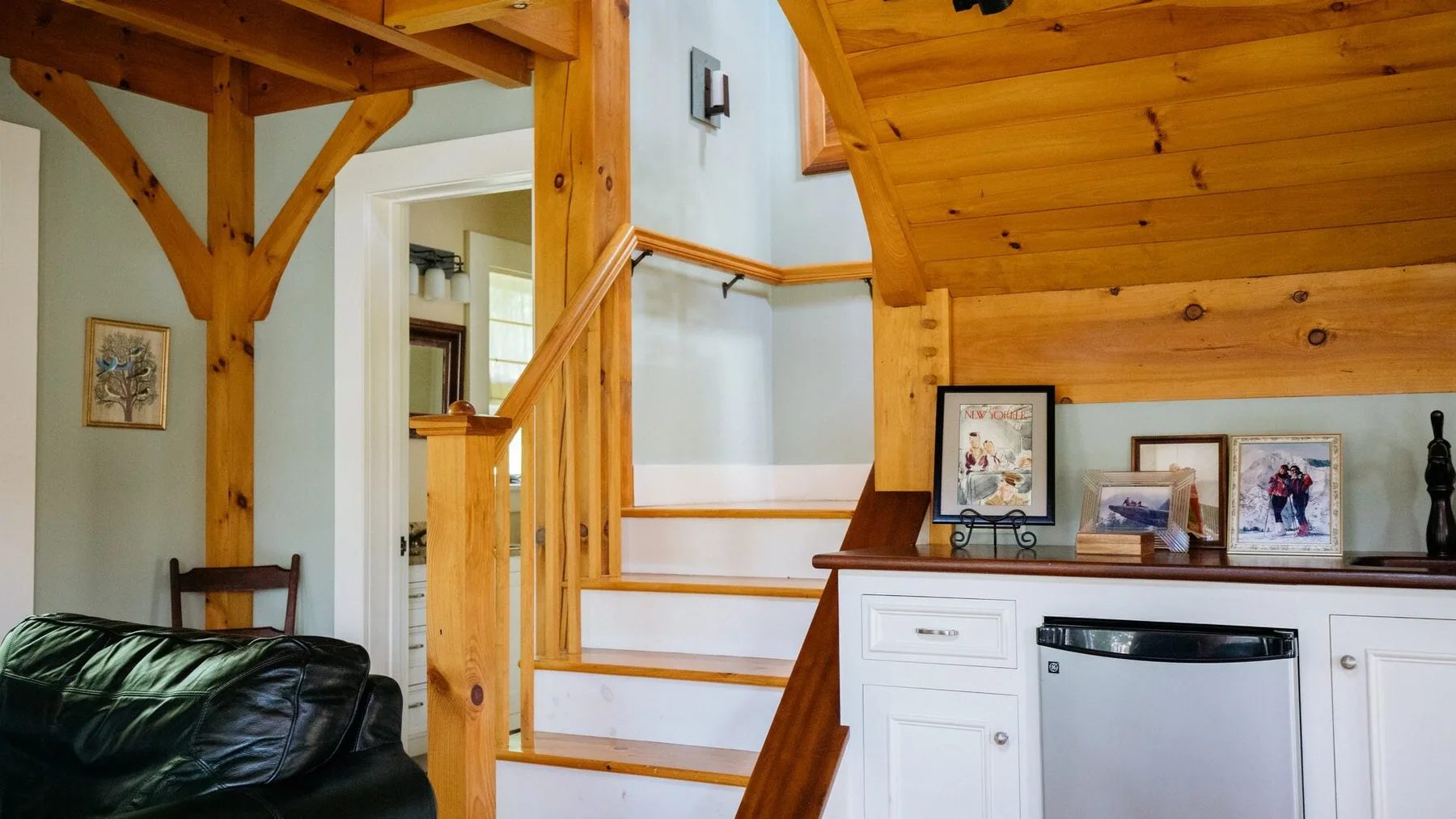 A wood-beamed living area with a staircase and kitchen cabinetry.