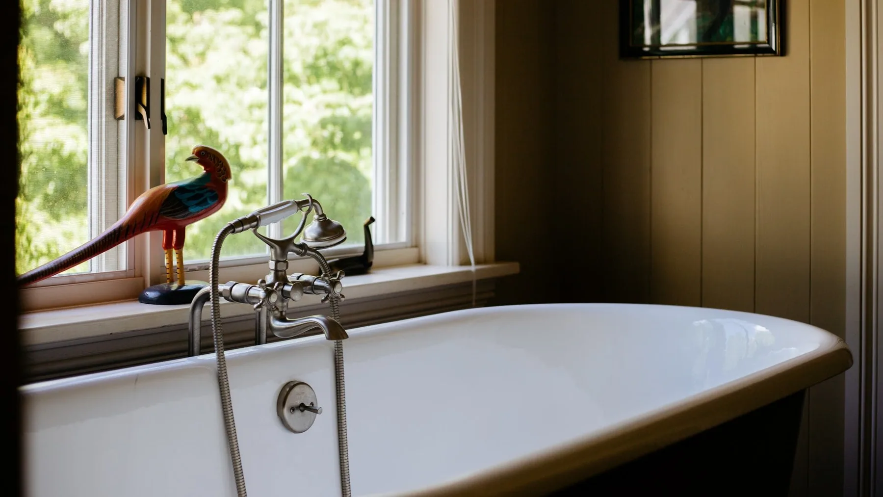 A bathtub sits beside a window, with a faucet and a decorative bird figure.