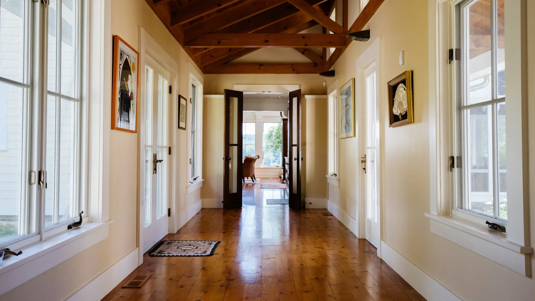 A long interior hallway with wood floors, large windows, and exposed ceiling beams.