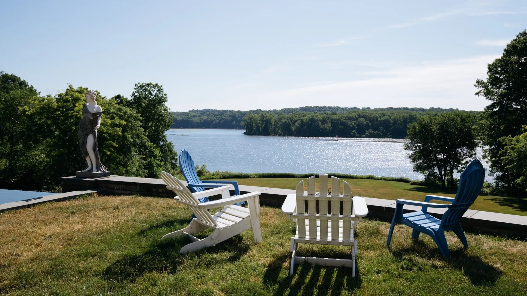 Outdoor seating overlooks a lake, with a statue standing beside the lawn.