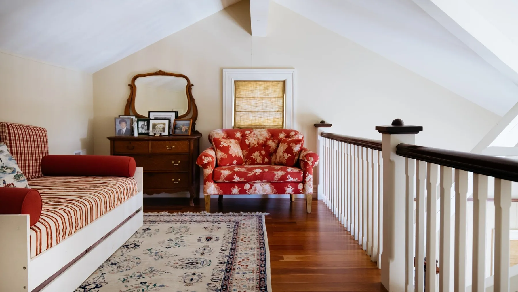 An upstairs sitting area with patterned seating, a dresser, and a railing.