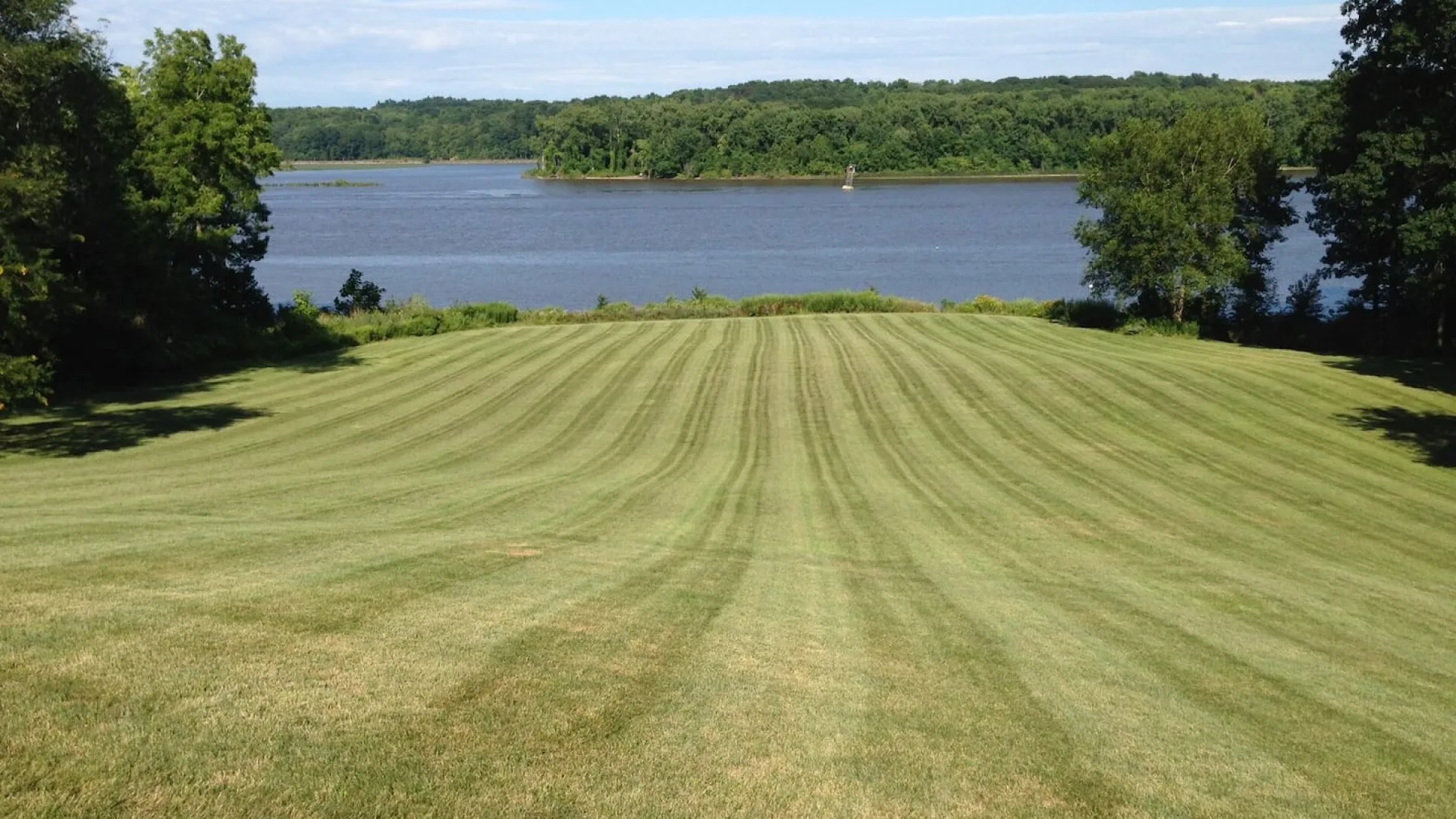A freshly mown lawn slopes toward a broad river, with trees along the banks.
