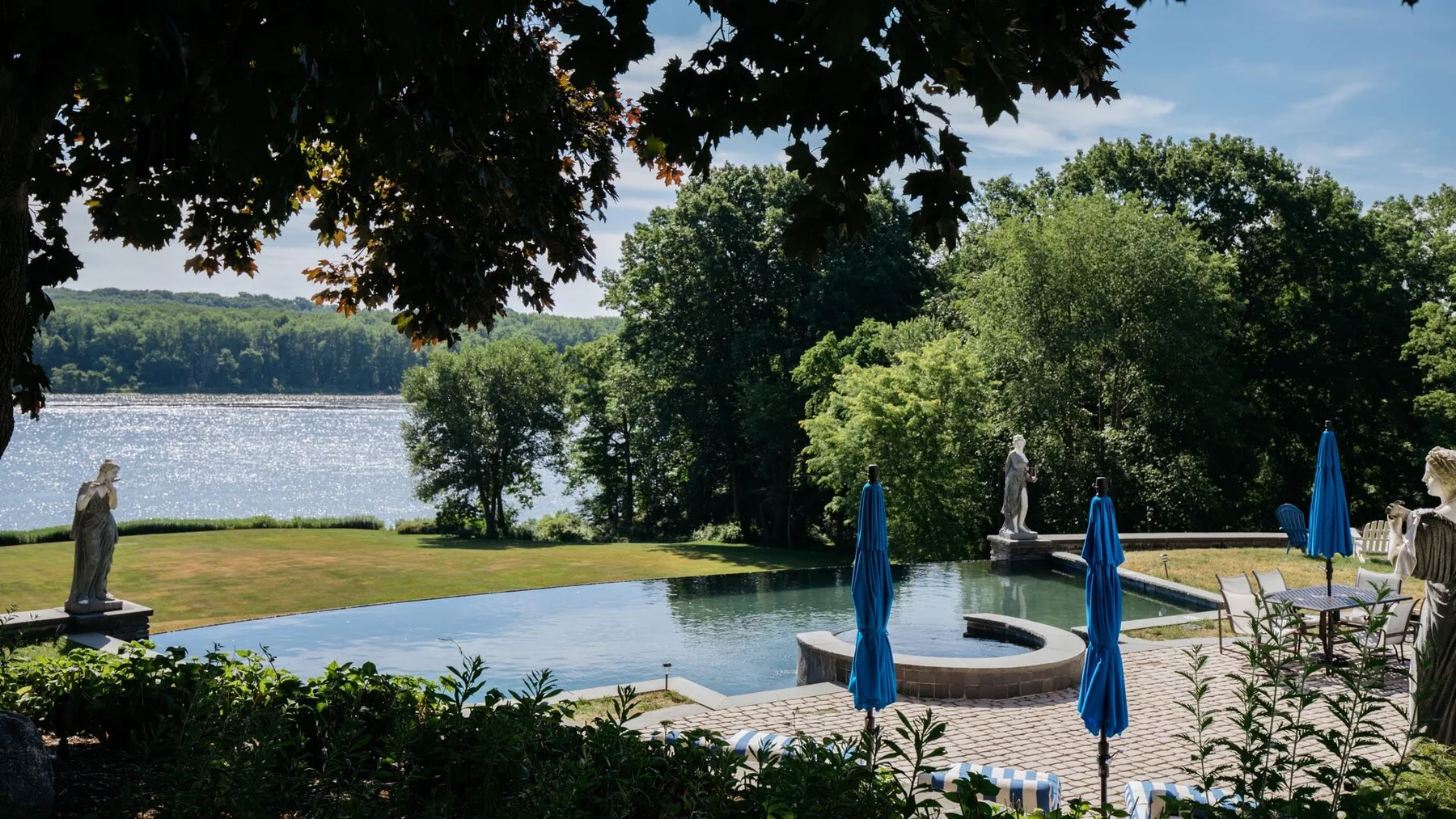 Una piscina al aire libre junto a un lago, rodeada de árboles y jardines.
