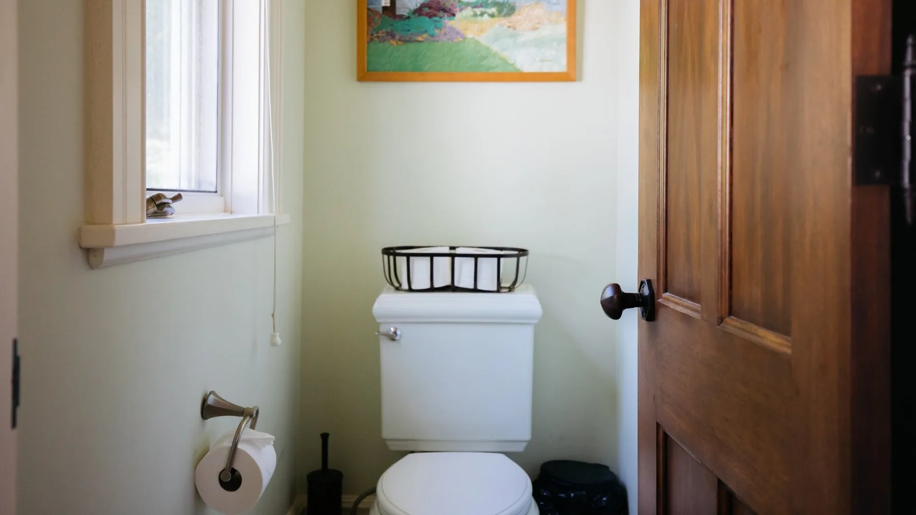 A bathroom with a toilet, a window, and a wooden door.