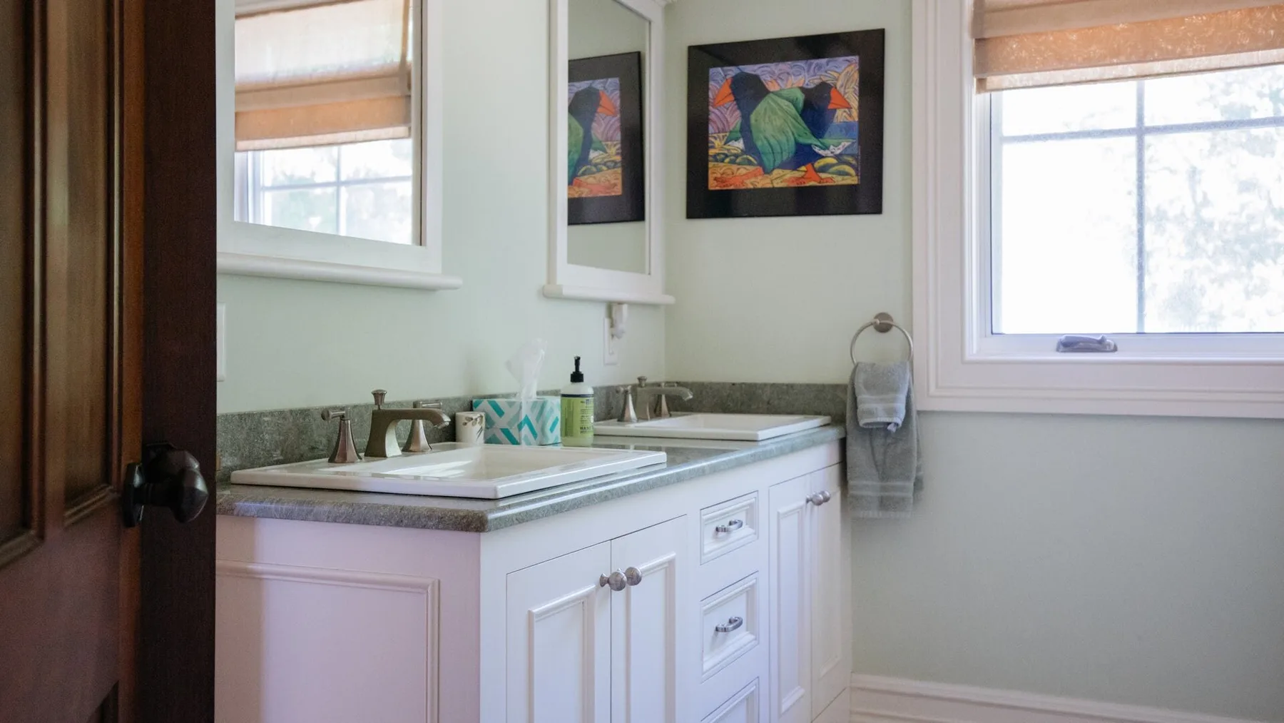 A bathroom vanity with a sink sits beneath framed artwork and beside a window.