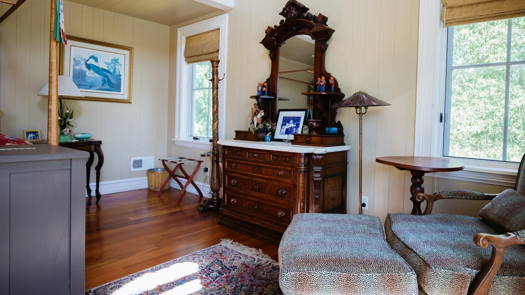 A bright sitting room with a wooden dresser and upholstered seating beside large windows.