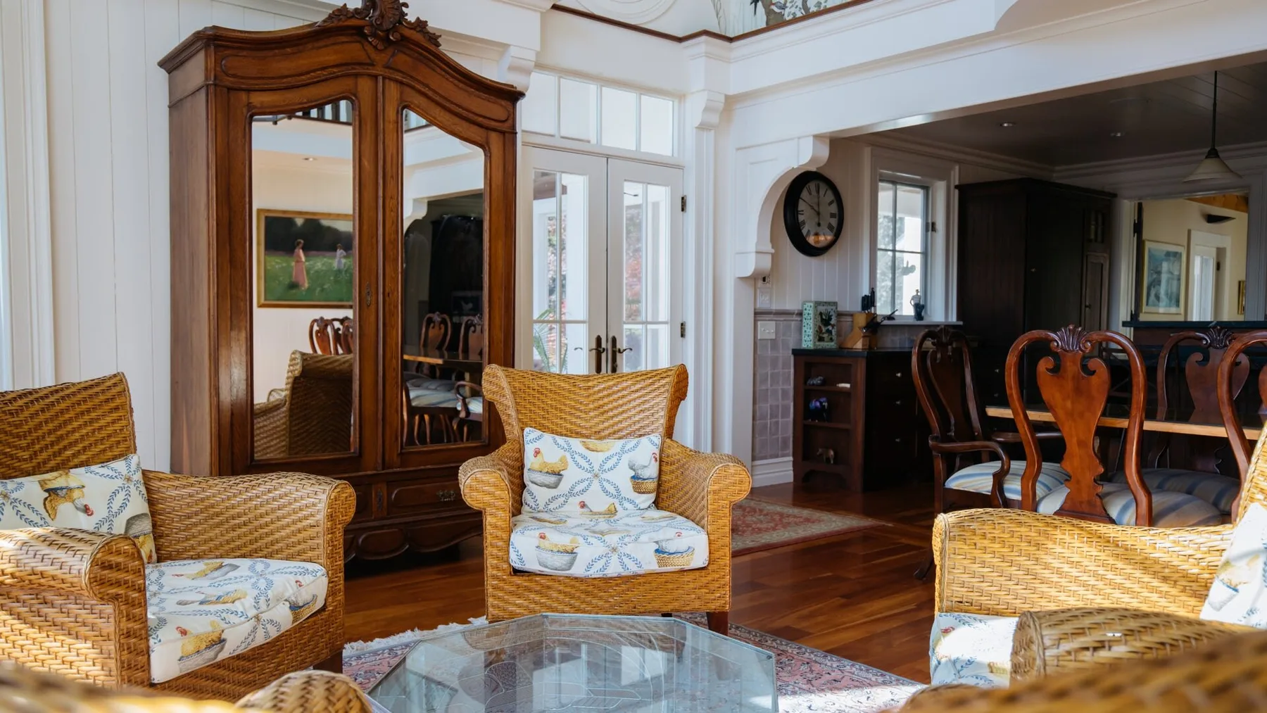 A bright living room with armchairs, a mirrored wooden cabinet, and a glass coffee table.