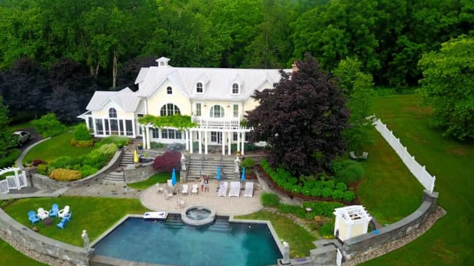A large white house overlooks a landscaped yard with a swimming pool.