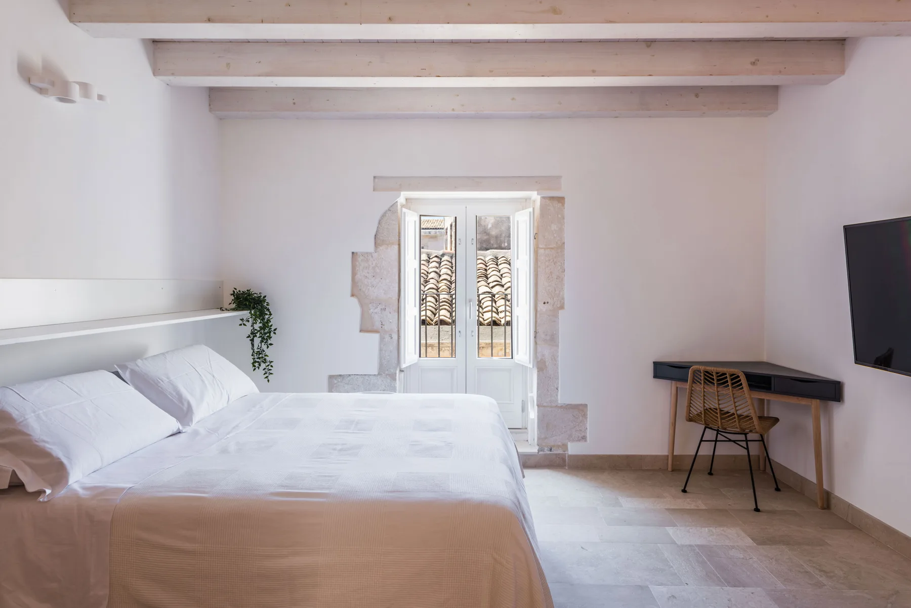 A bright bedroom with a bed, a desk, and a window.