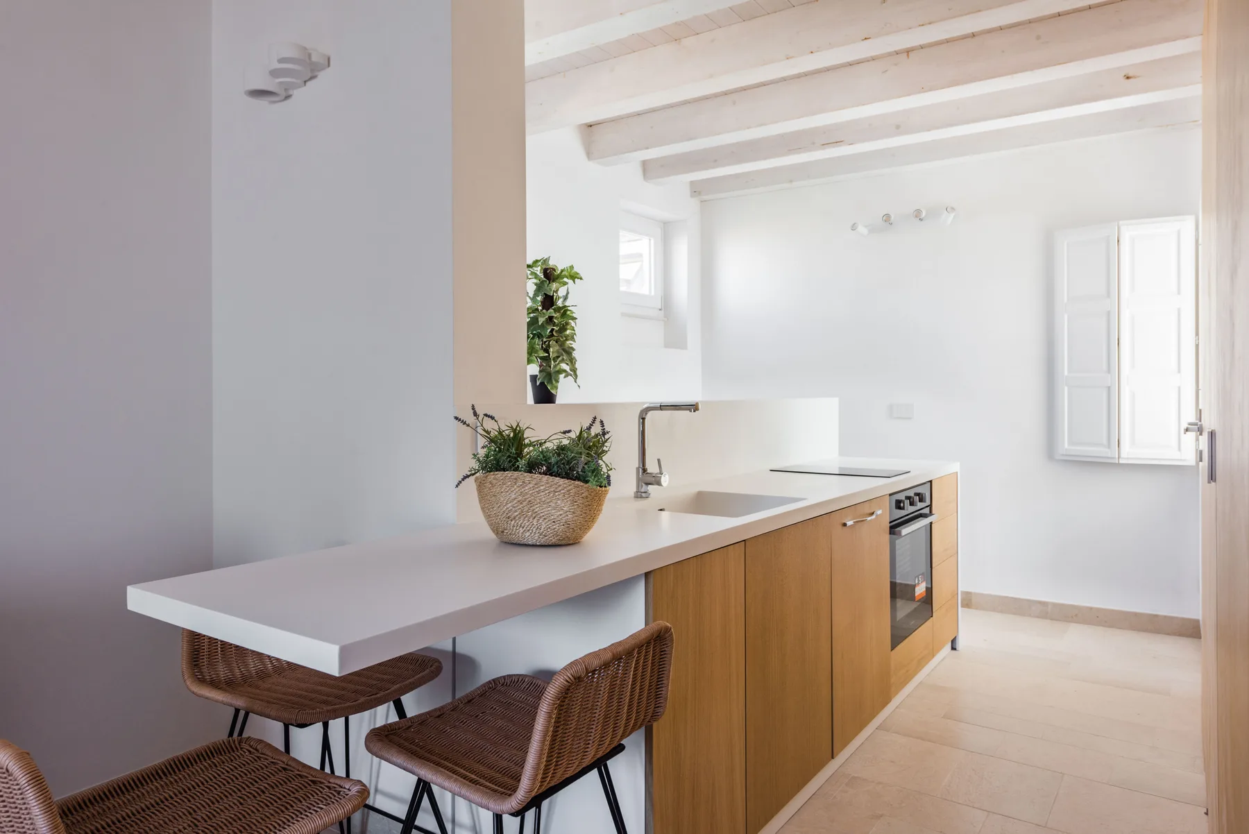 A bright kitchen with a long counter, wooden cabinets, and woven seating.