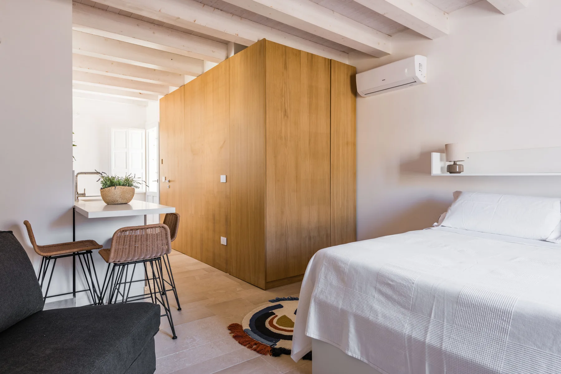 A bright bedroom with a bed, wooden partition, and small dining area.