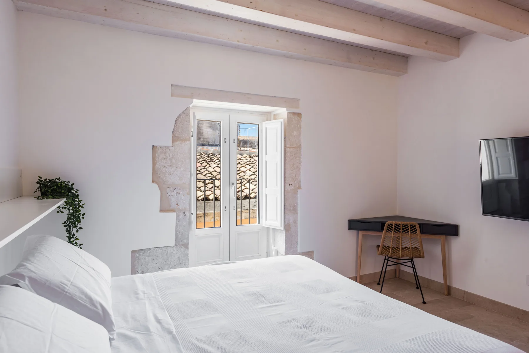A bright bedroom with a white bed, a desk, and a window.