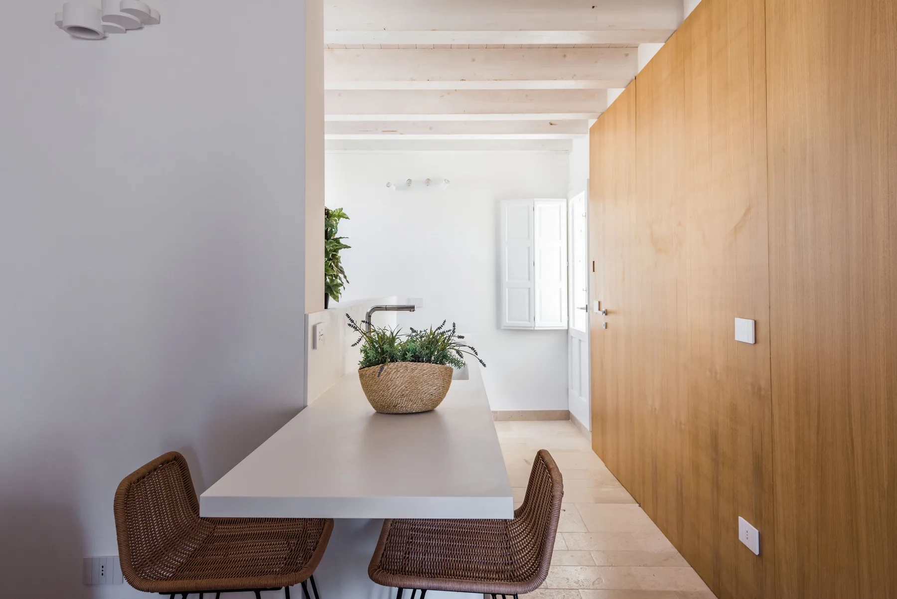 A bright dining area with a table, woven seating, and a long wooden wall.