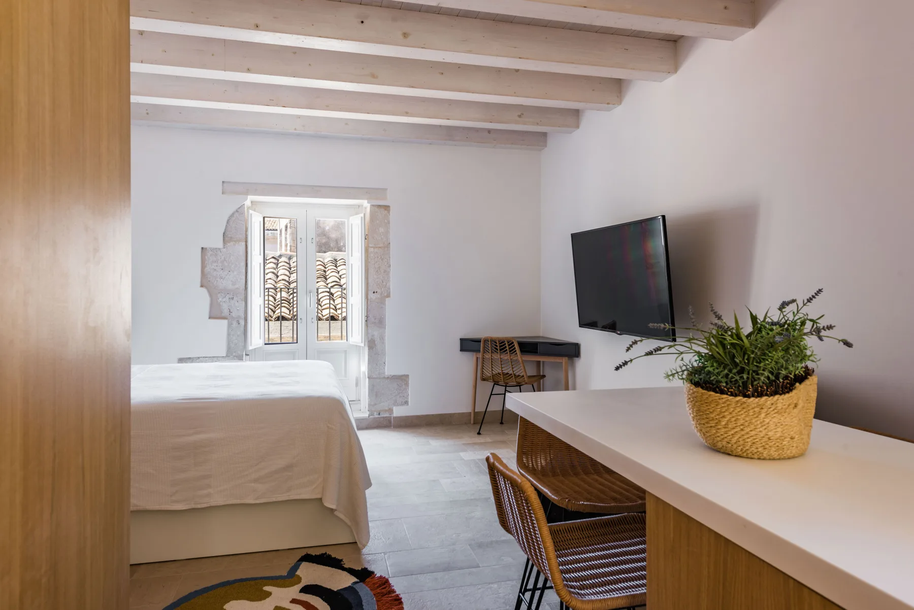 Bedroom with a bed, desk, and television beside a bright window.