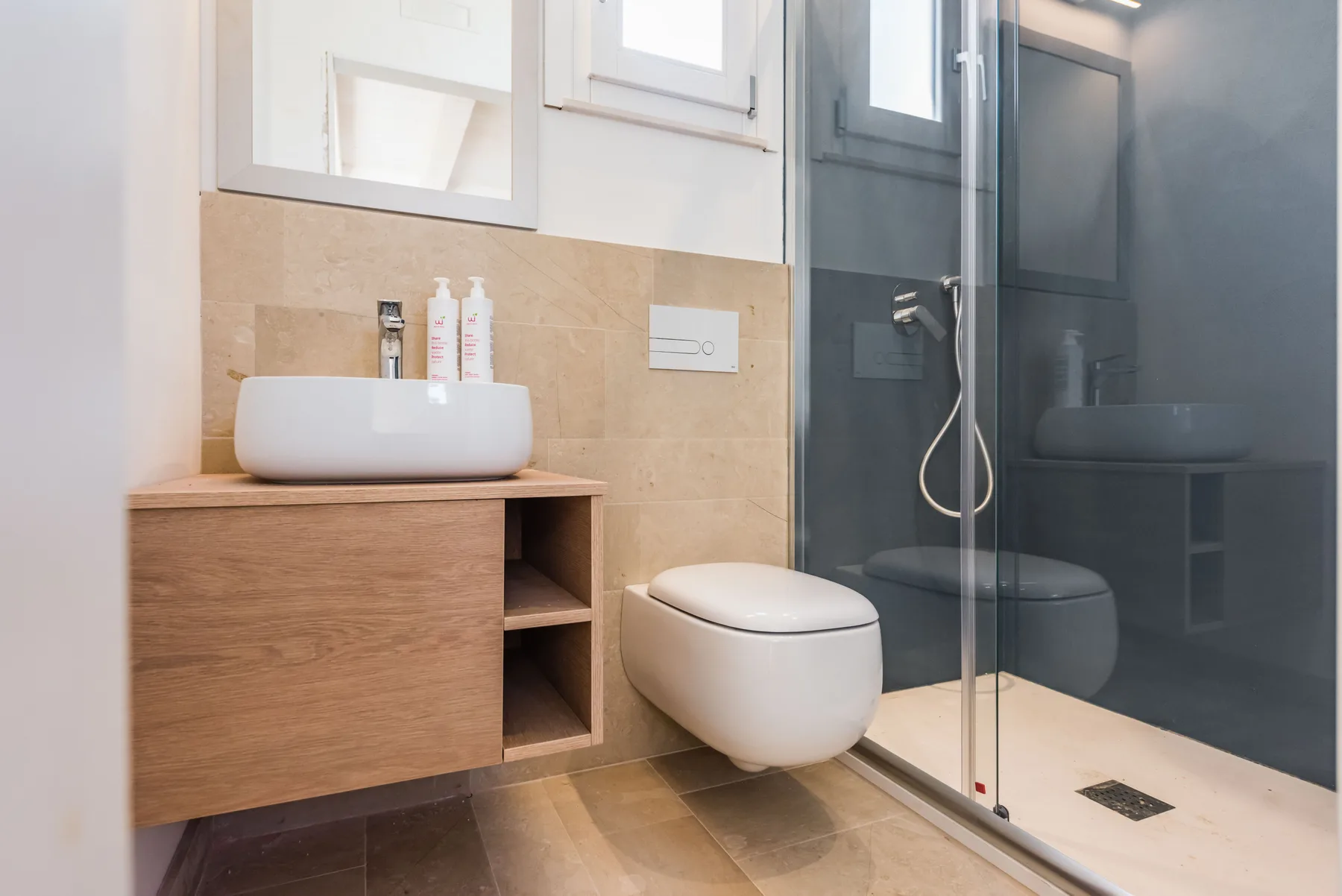 A modern bathroom with a vessel sink, wall-mounted toilet, and glass shower.