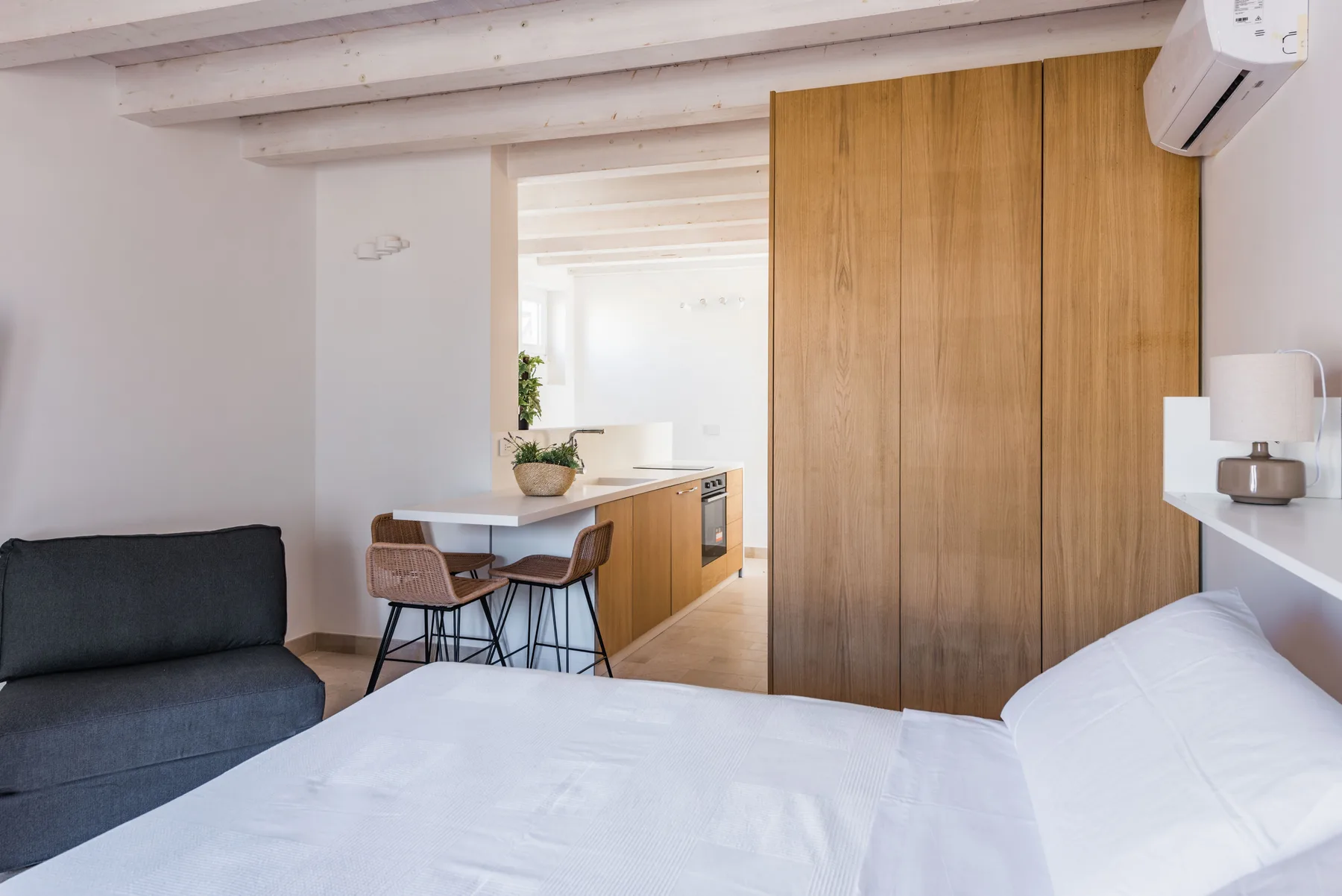 A bedroom with a bed, seating, and a small kitchen area.