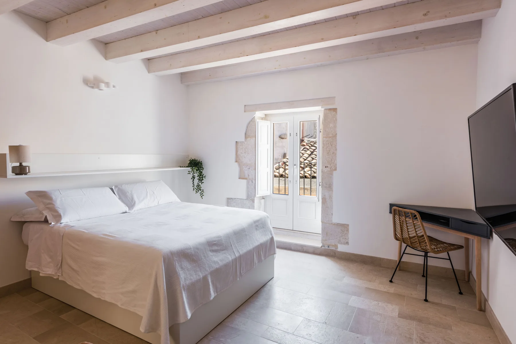 A bright bedroom with a large bed, exposed ceiling beams, and a desk.