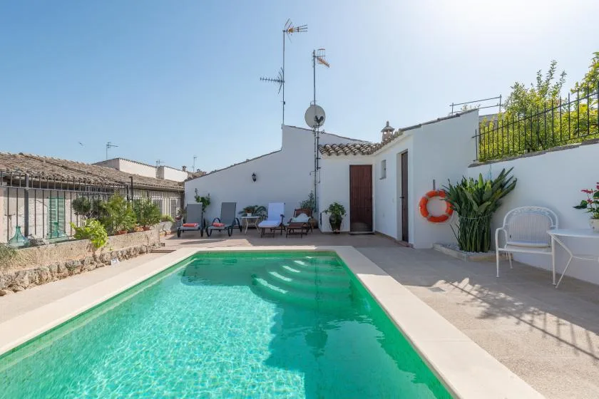 A swimming pool fills a sunny courtyard beside a white building.
